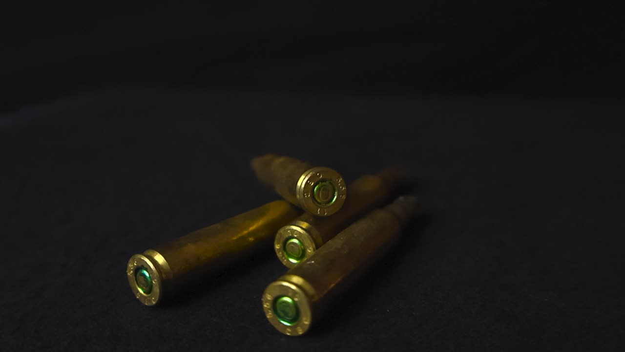 Close up view of shiny bronze and golden colored high caliber military rifle weapon ammo or bullets in front and on a black studio background. The blanks are unfired and video spins around them