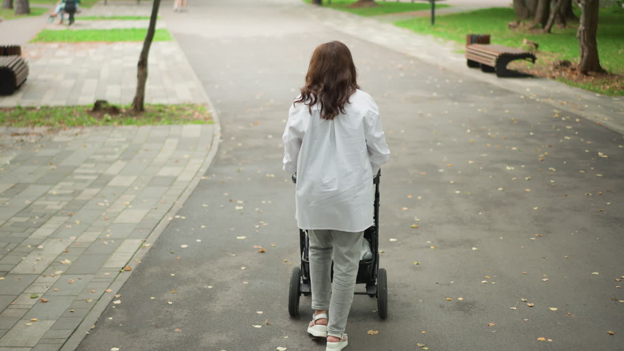 Betreuungsperson schiebt Kinderwagen. Kinderbetreuung auf friedlichem Parkweg. Sanfte Betreuungsperson geht sicher mit Baby spazieren. Idyllische Szene einer fürsorglichen Betreuungsperson, die gemächlich auf einem Parkweg schlendert.