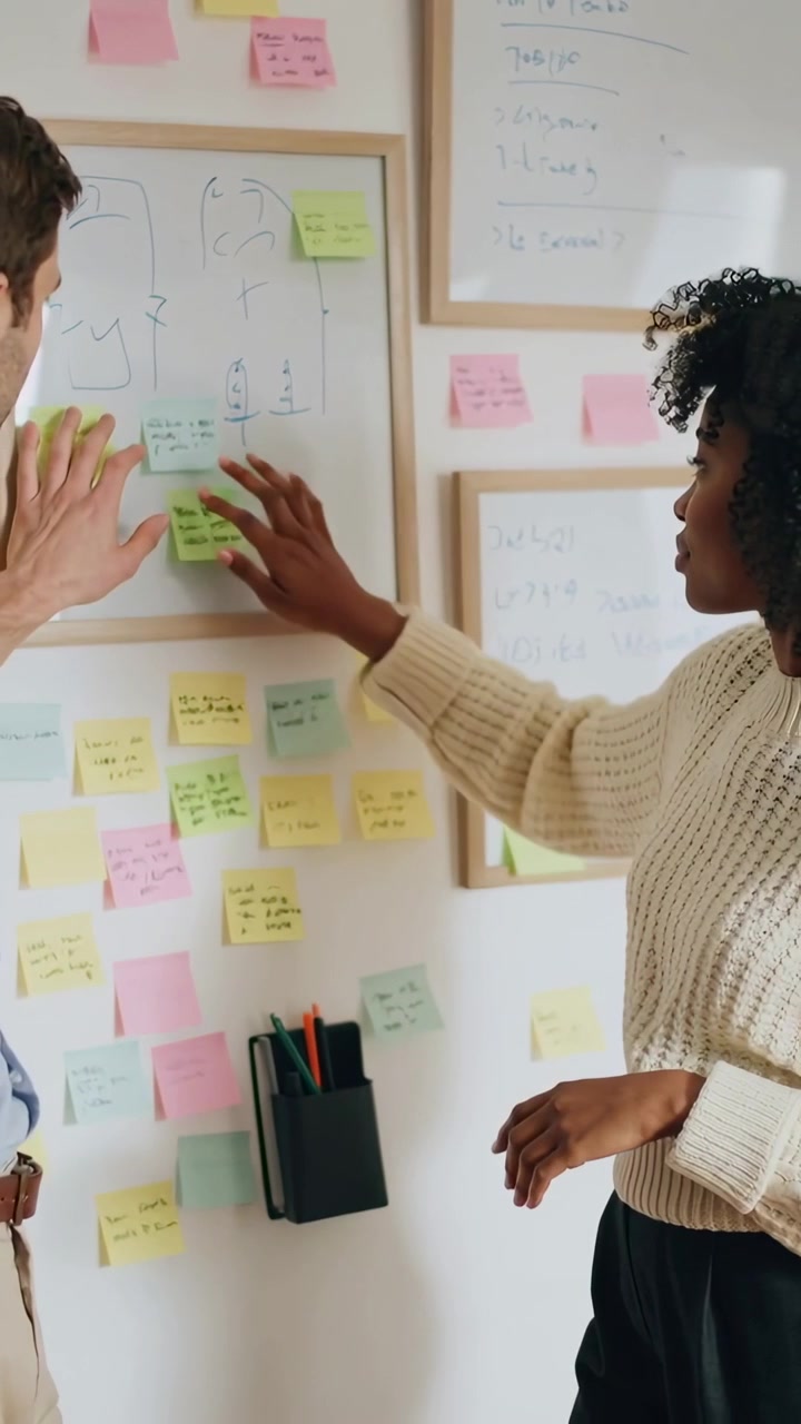 Vertical video: Pointing man guiding woman in office clothes moving sticky notes on board to plan