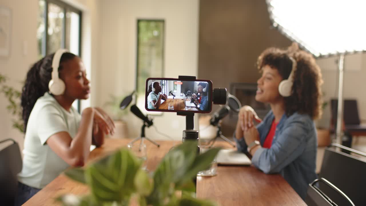 Diverse female podcasters testing mics starting chat after smartphone flashes red at wooden table