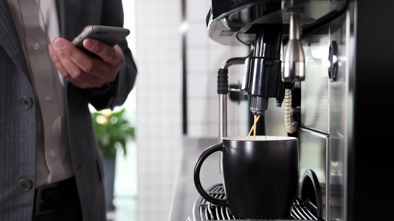 Handsome businessman in formal suit using mobile phone waiting for coffee until it’s ready. Male typing browsing chatting smartphone at workplace indoor confident entrepreneur financier or broker