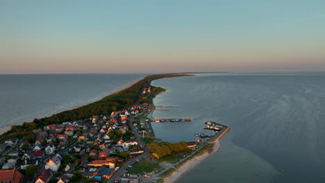 aerial view of kuźnica, poland, showing a coastal village with houses, piers, and boats along a narrow strip of land between two bodies of water during sunset