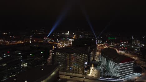 Helsinki-winter-night-aerial-over-Kansalaistori-Square,-search-lights