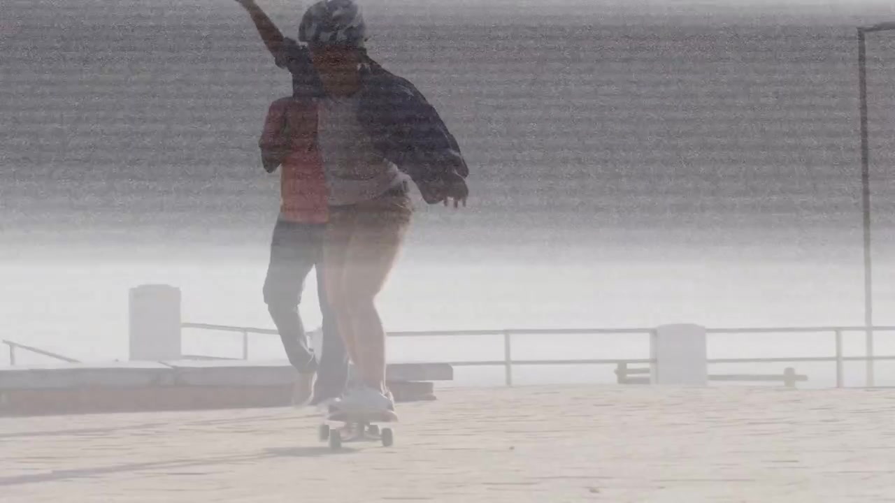 Barn sparker fra på skateboard og får balansen på strandpromenaden, voksen støtter trening for ferdighet.