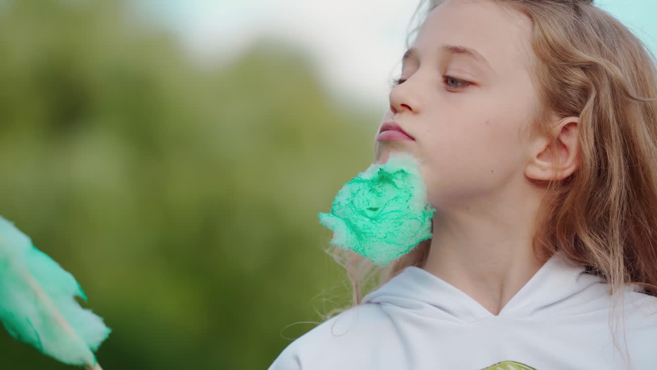 Funny girl with green cotton candy outdoors. Portrait of a little blonde girl eating sweet candyfloss. Child making funny face with a cotton candy.
