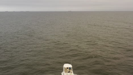 an aerial view of a small, white fishing boat speeding in the deep, green atlantic ocean by long island, ny