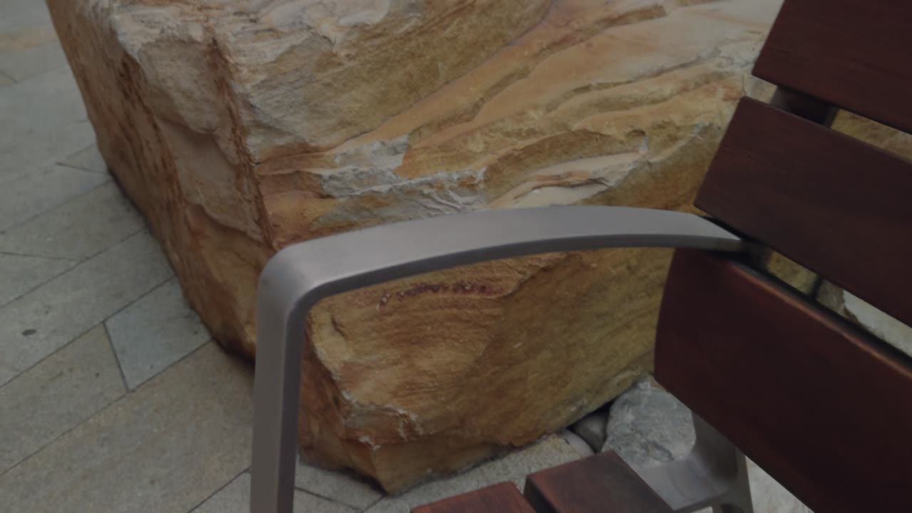 Panning along a wood and metal bench with faint stream behind in parkway