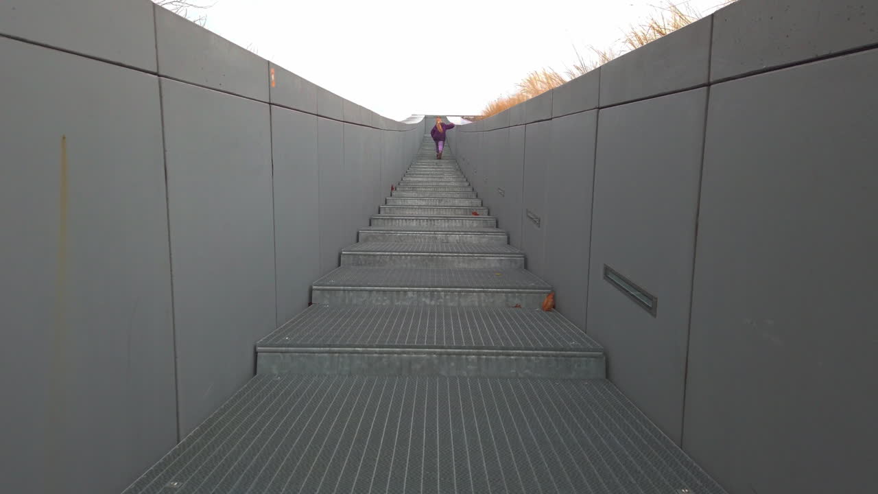 A young girl in a purple jacket ascends the modern metal stairs of the Museum of Ethnography in Városliget, Budapest. A cinematic shot capturing childhood curiosity within minimalist architecture