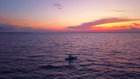 una toma dramática de un dron de un kayakista solitario deslizándose lentamente hacia una puesta de sol colorida