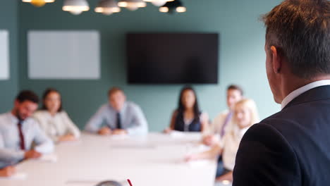 mature businessman addressing group meeting around table at graduate recruitment assessment day