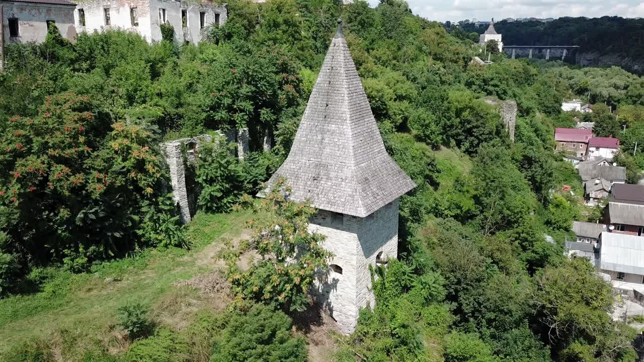 Aerial pan left towards Kushnirska Tower surrounded with greenery and old buildings at Kamianets Podilski,Ukraine.
