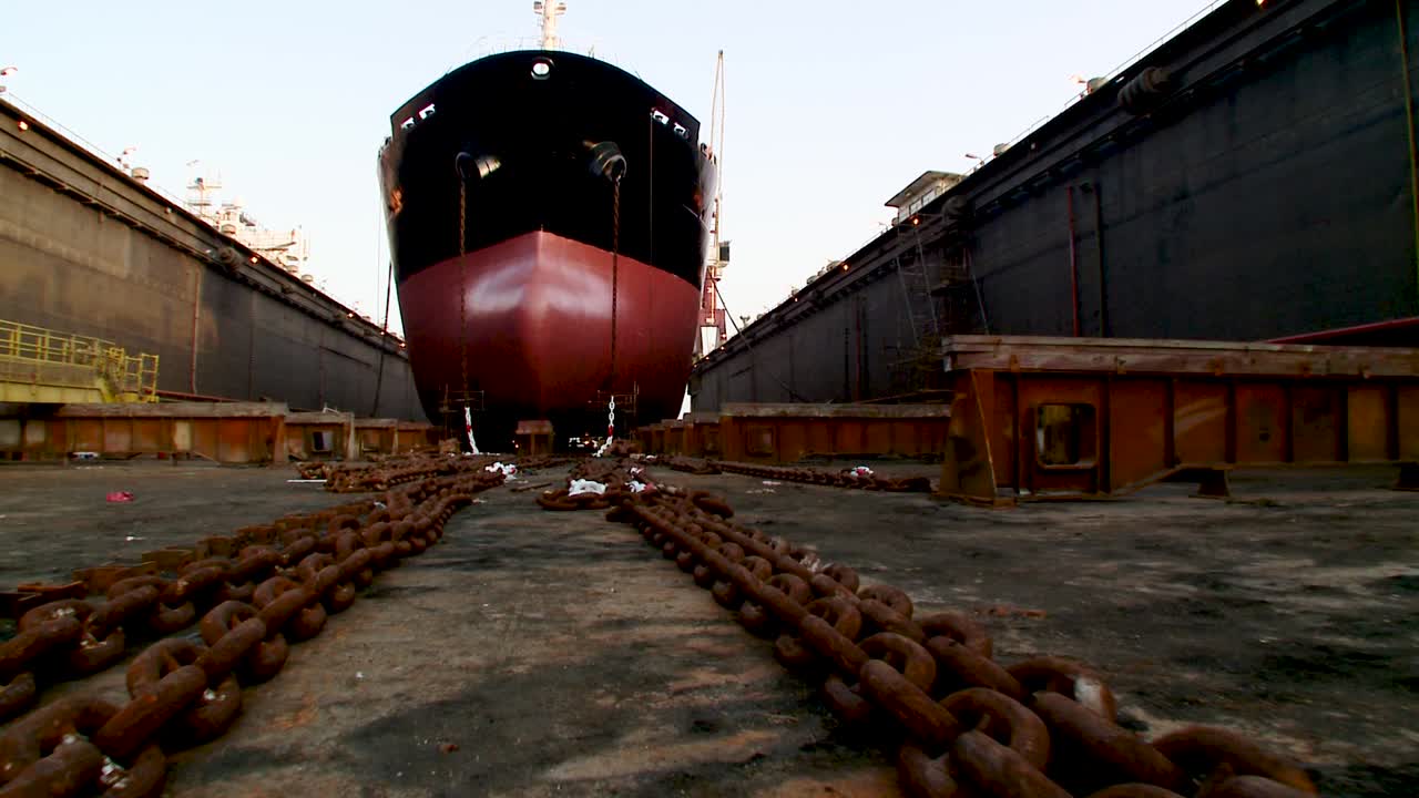 Crane panning rtl and tilting up shot of an oil supertanker in dry dock. Shot from floor level