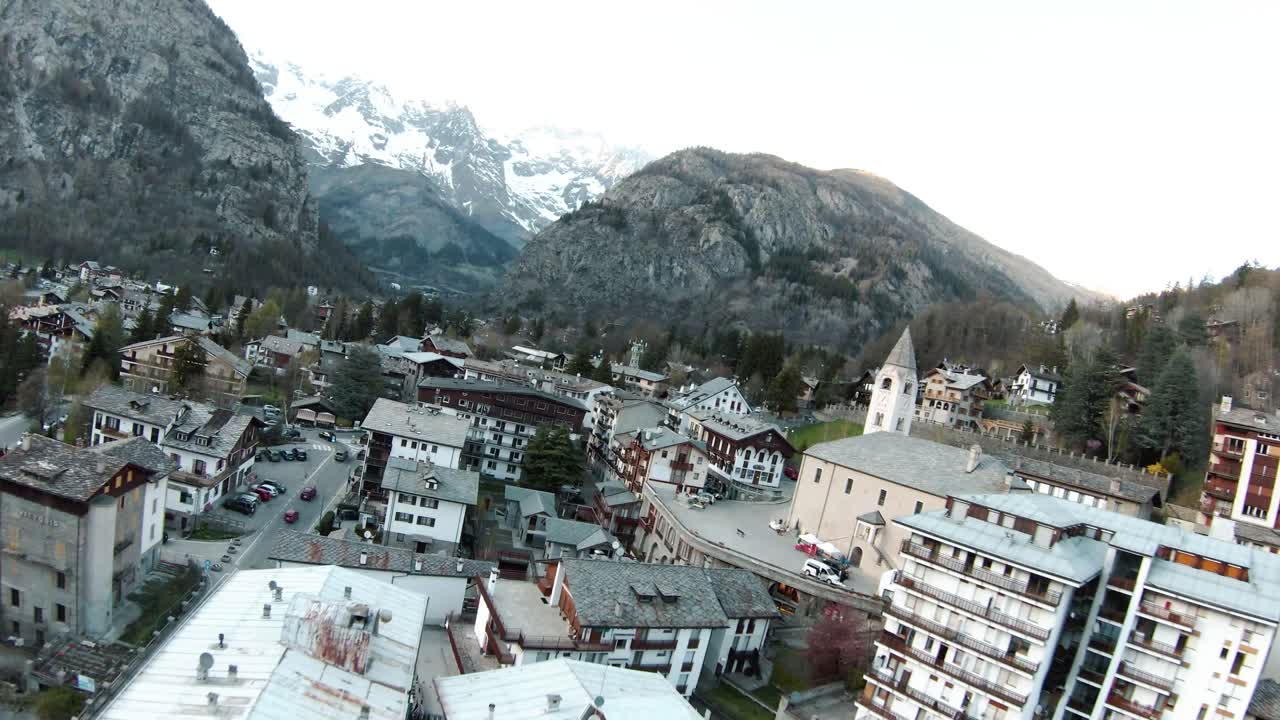 fpv drone aéreo sobre el centro turístico de montaña alpina y la iglesia de courmayeur, valle de aosta, italia, mont blanc monte bianco, volando sobre casas