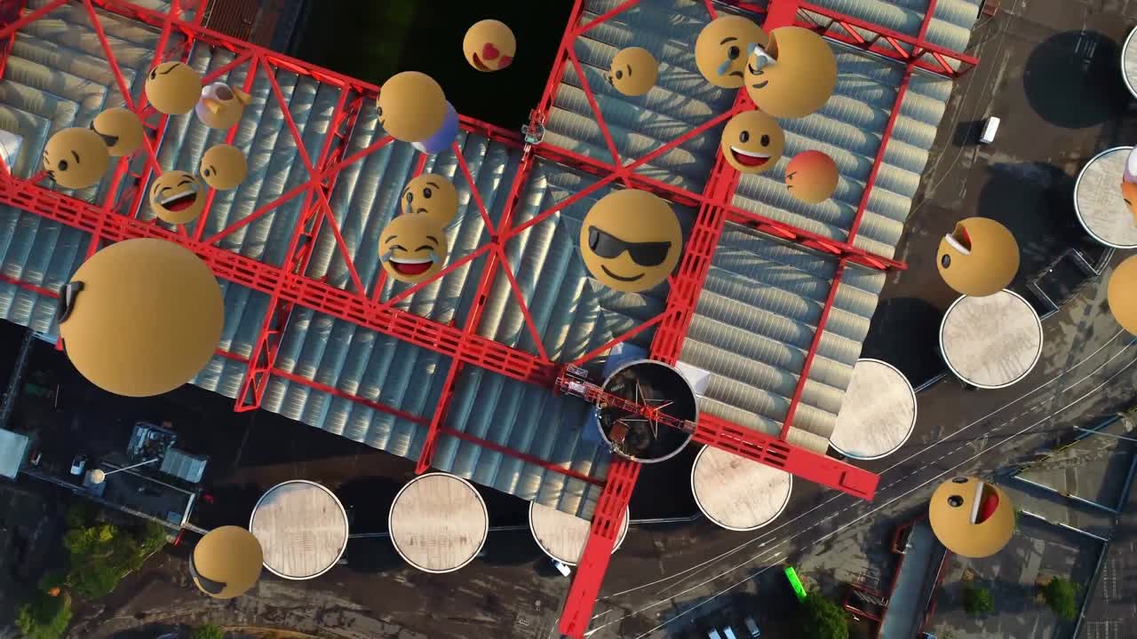 composición digital de varios emojis de cara flotando contra la vista aérea del almacén en la ciudad