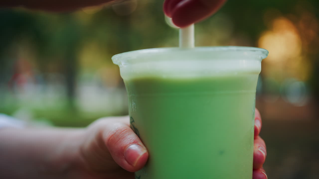 Close up of woman's hand holding an iced matcha latte outdoors
