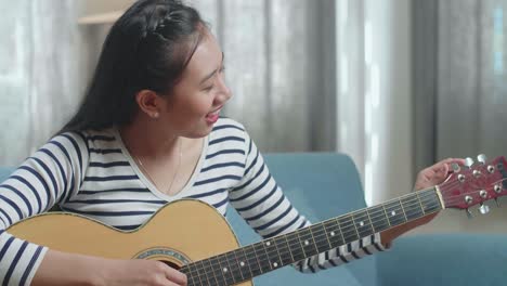 close up of asian woman learning pulling strings of guitar by laptop at home