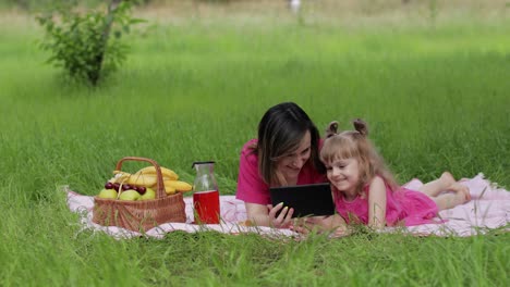 Family-weekend-picnic.-Daughter-child-girl-with-mother-study-lessons-on-tablet.-Distance-education