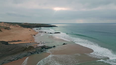 aerial blue waves rolling to sandy beach framed by rocky cliffs. overcast sky