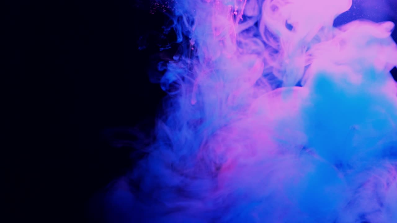 Color splashes of ink isolated on black background. Abstract paint in water, photographed in motion. Swirling colorful drops cloud.