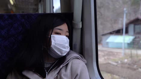 Triste-Chica-Asiática-Con-Mascarilla-Mirando-Desde-La-Ventana-Del-Tren-Al-Paisaje