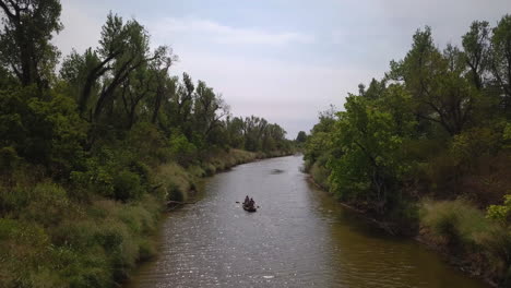 toma aérea de un hermoso río dentro de un área forestal en una hermosa naturaleza con árboles y una canoa flotante con dos personas remando a lo largo de la orilla