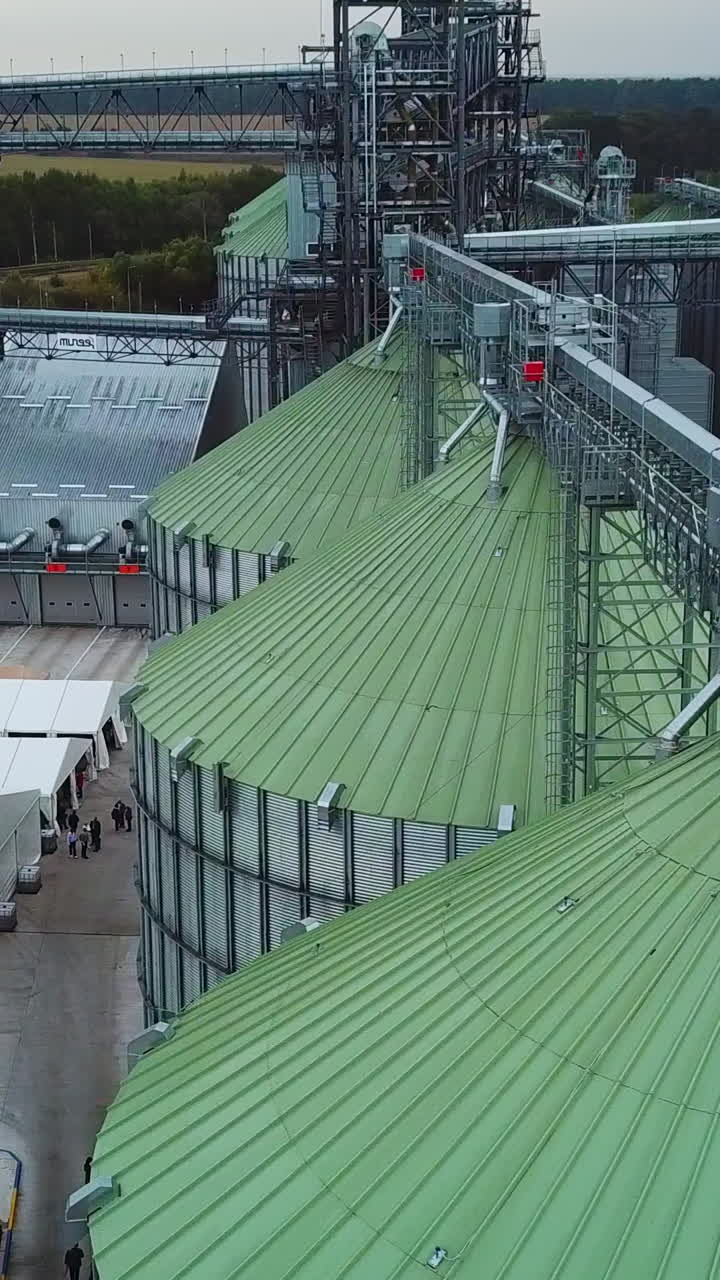 Light green roofs of tanks joined by metal supports. Railroad going through the plant territory and white tents nearby. Top view. Vertical video