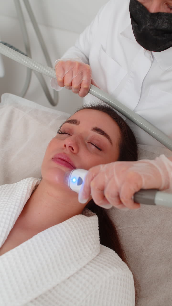 Woman receives rf lifting facial massage therapy from cosmetologist using professional equipment