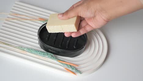 colocando a mano una barra de jabón en un plato de jabón negro en una bandeja decorativa.