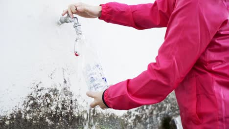 person filling a glass bottle of water from a natural tap