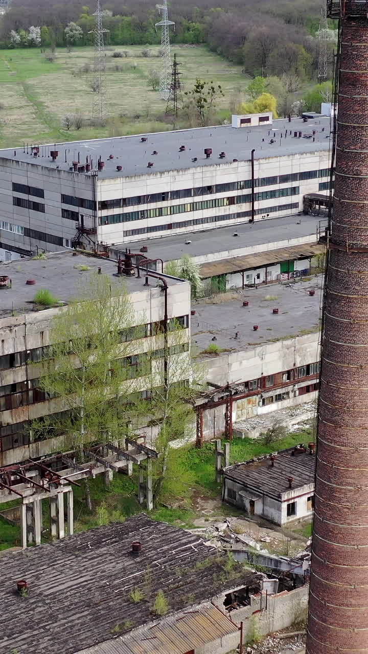 Panoramic view of an old factory. Abandoned territory of industrial plant with large brick pipe. Ruined manufacting in springtime. Aerial view. Vertical video