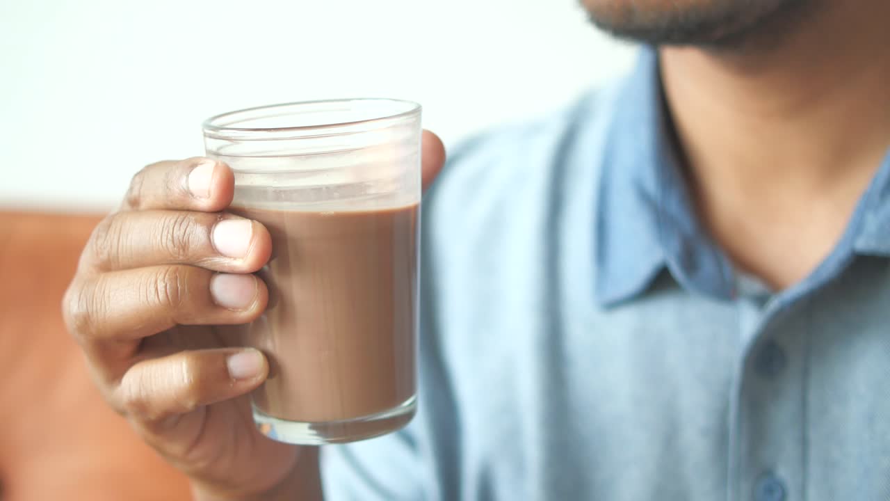 Un uomo beve un bicchiere di latte al cioccolato.