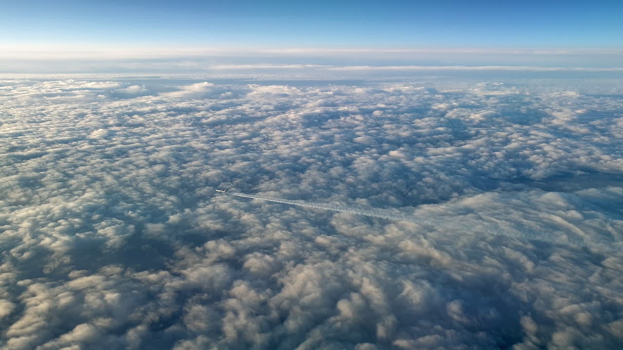 Incredible view from the cockpit of an airplane flying high above the clouds leaving a long white condensation vapour air trail in the blue sky
