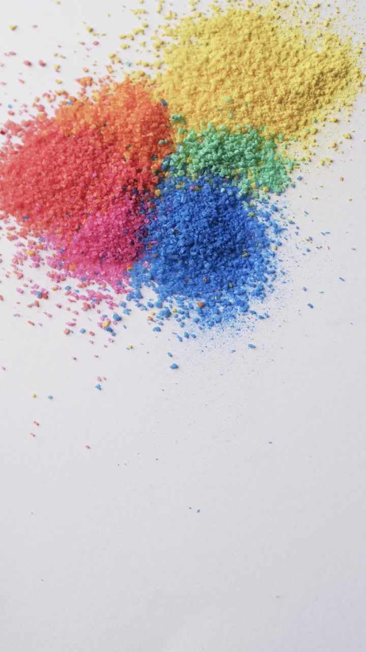 Video verticale in primo piano di granelli di sabbia multicolore e spazio per il testo su sfondo bianco