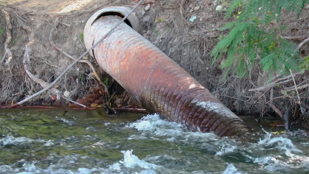 A Metal Irrigation Pipe In A River Flowing Through The Forest Close Up 20 Second Video.