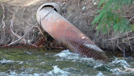 a metal irrigation pipe in a river flowing through the forest close up 20 second video.