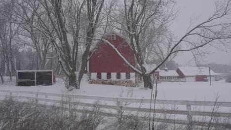 Snow-covered red barn in Minnesota, surrounded by trees and a white fence in winter