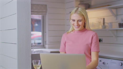 woman putting in wireless earbuds standing at kitchen counter making video call on laptop