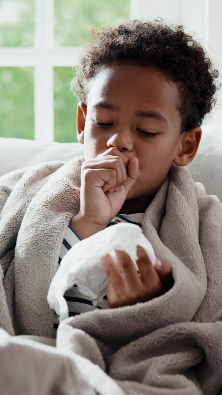 Sick Young Boy Coughing and Blowing Nose at Home