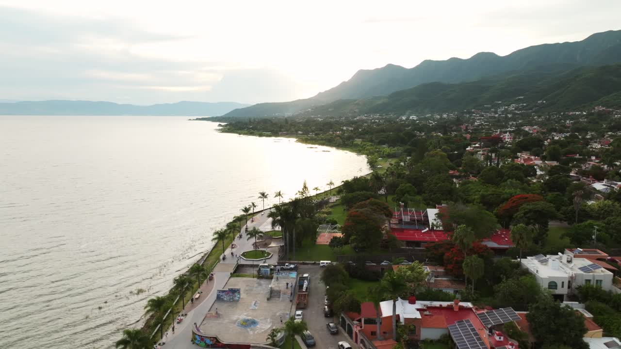 Malecon de Ajijic City in Mexico during foggy day. Palm trees at promenade of city. Sunset time in Mexico. Aerial orbit wide shot.