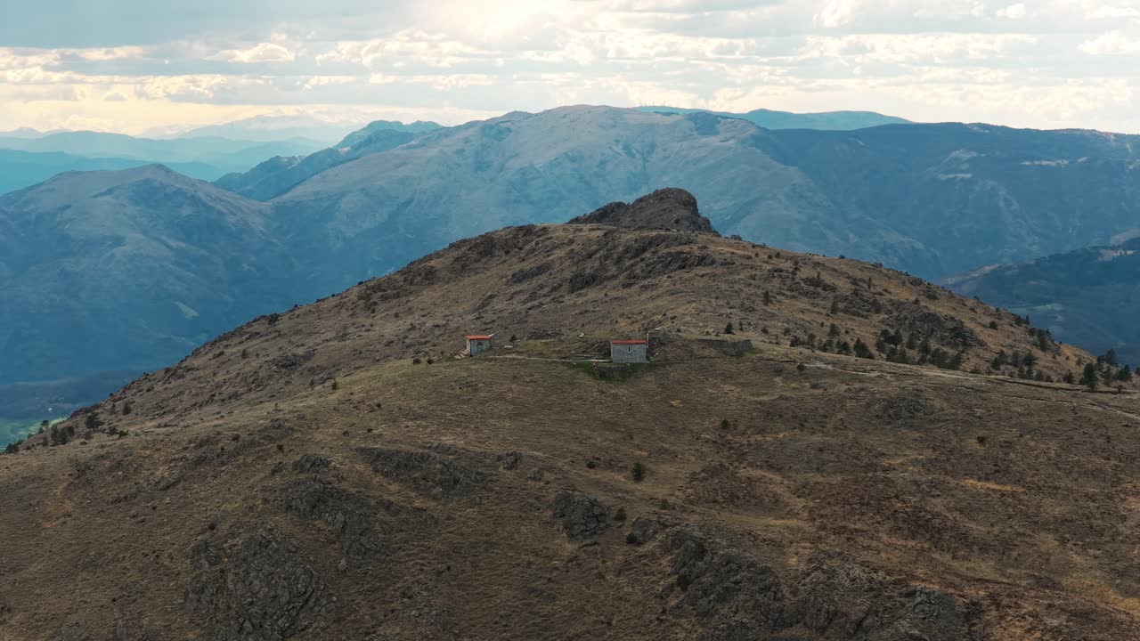 Two small, isolated huts on rugged Praglia mountain ridge under cloudy sky at dusk, evokes solitude, Ligurian Apennines, Italy. Aerial drone panoramic view