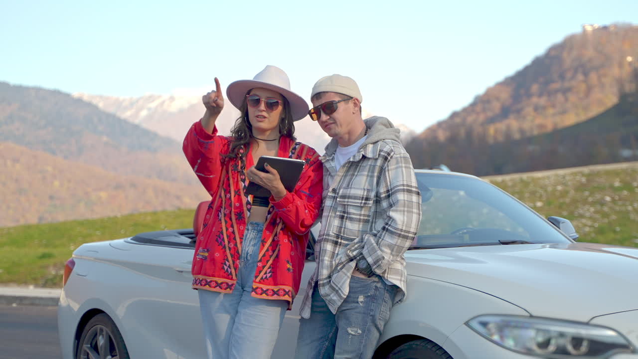 pareja usando tableta por un coche descapotable en las montañas