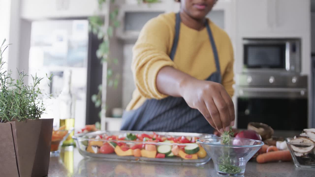 sección media de una mujer afroamericana en delantal sazonando verduras en la cocina, en cámara lenta