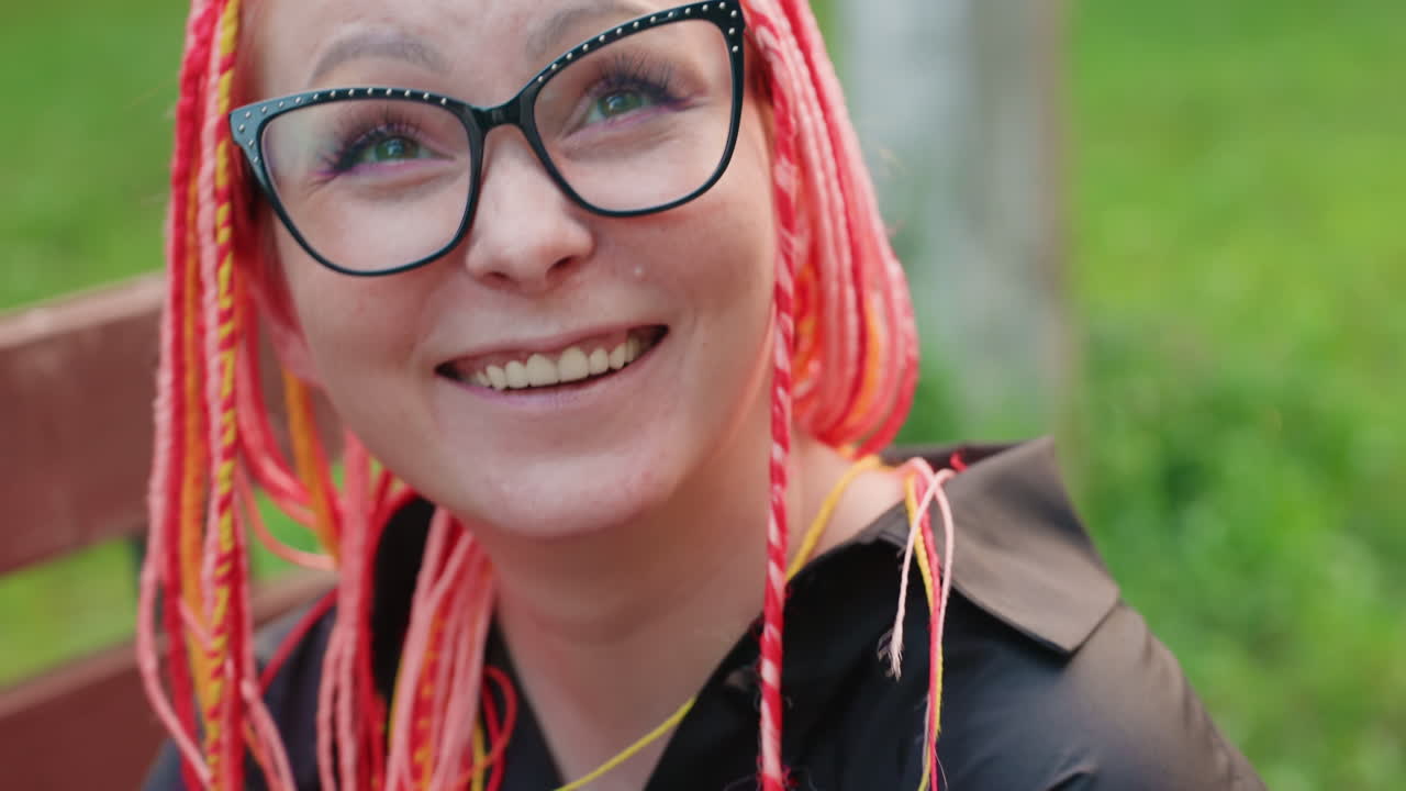 mujer alegre con trenzas vibrantes sonriendo al aire libre; mujer jovial con cabello llamativo disfrutando de un día soleado en el parque; escena armoniosa de una mujer riendo con trenzas coloridas en un parque verde y exuberante