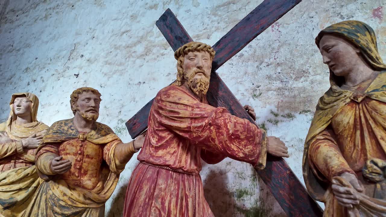 Biblical sculpture depicting Jesus carrying cross with figures in background