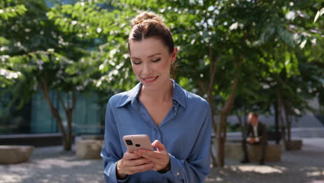 gerente despreocupado enviando mensajes de texto por teléfono móvil sentado en la plaza de la ciudad soleada de cerca.
