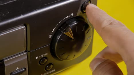 angled close-up shot: a hand manipulates the knob of a vintage vhs vcr, commanding the videotape motor to perform various actions such as fast forward and rewind