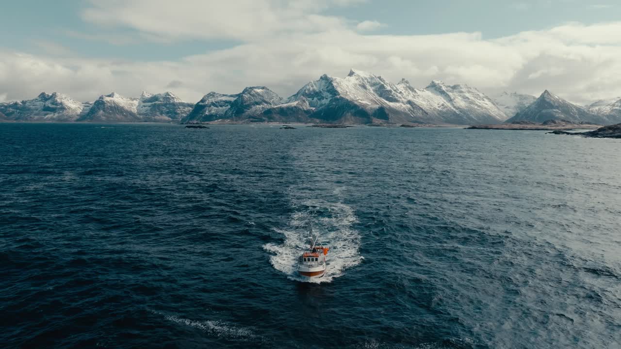Aerial View of Fishing Boat Navigating In The Sea With Snowy Mountain Range In The Background.
