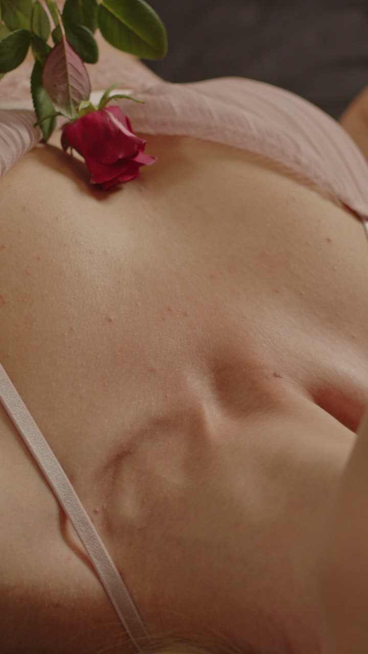 Bellissimo primo piano verticale di una rosa rossa che sfiora delicatamente la pelle di una donna in lingerie