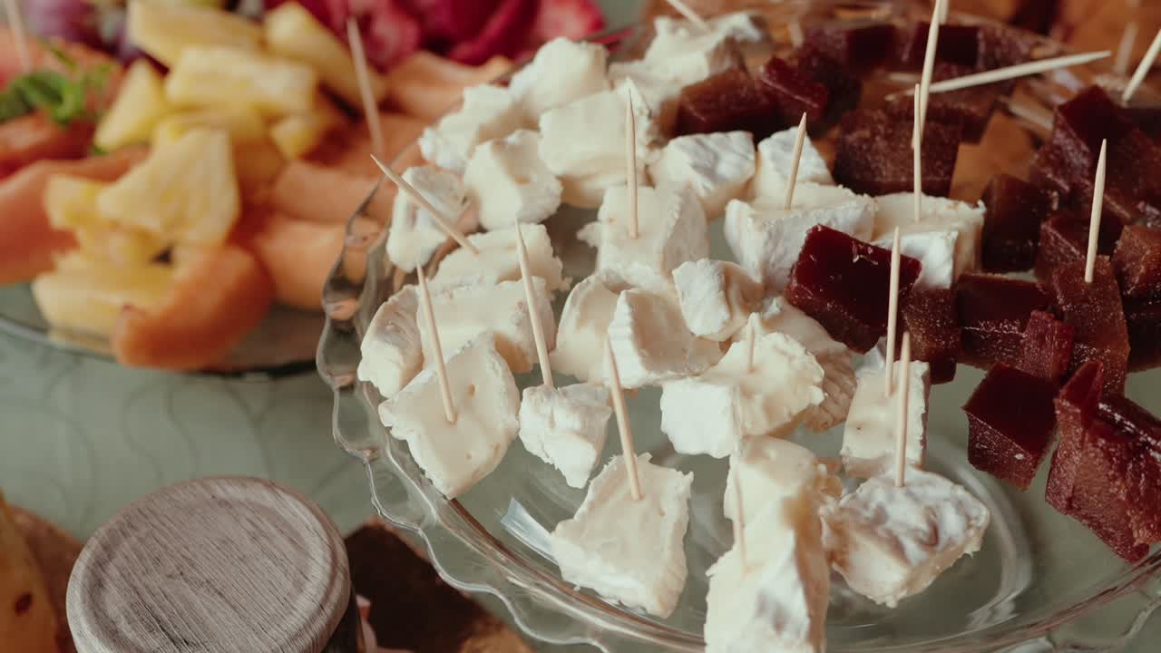 close up of creamy cheese and quince paste cubes served with toothpicks on a clear tray