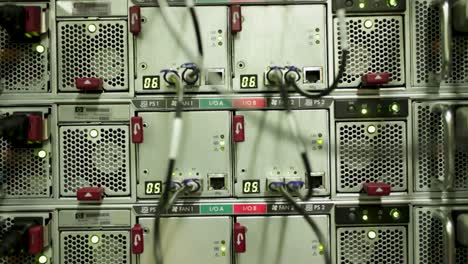 Silver-server-row-with-fans-and-black-cables-in-datacenter,-lowering,-close-up